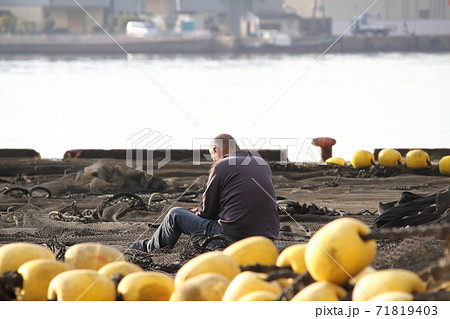岸壁に広げた漁網を手入れする男性 71819403