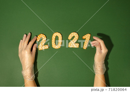 Woman hands in protective gloves, gingerbread cookies 2021 number on natural green background, pandemic new normal, 2021 New Year card, Christmas traditional sweetness, copy space 71820064