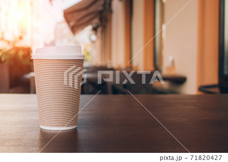 Mockup image of paper cup of coffee take-away, standing on wooden table with blurred cafe behind as background with copyspace. Coffee to go in recyclable paper cup Mockup image of paper cup of coffee take-away, standing on wooden table with blurred cafe behind as background with copyspace. Coffee to go in recyclable paper cup 71820427