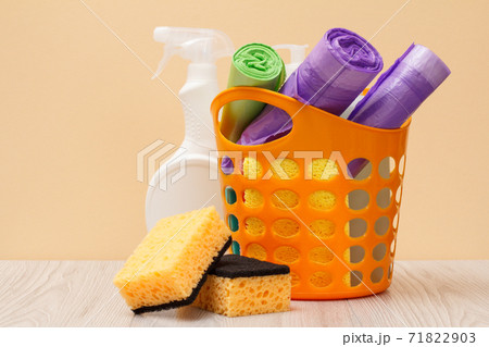Bottles of dishwashing liquid, basket with garbage bags and sponges on wooden desk. 71822903