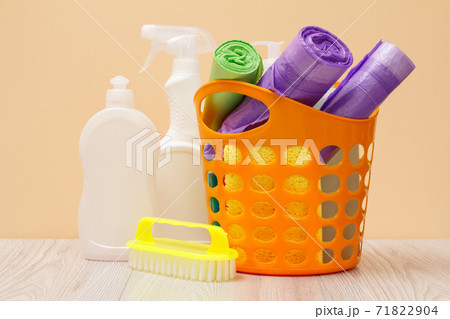 Bottles of dishwashing liquid, basket with garbage bags and brush on wooden desk. Bottles of dishwashing liquid, basket with garbage bags and brush on wooden desk. 71822904