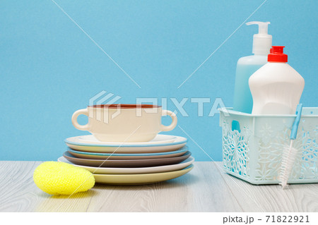 Bottles of dishwashing liquid in basket and plates on blue background. Bottles of dishwashing liquid in basket and plates on blue background. 71822921