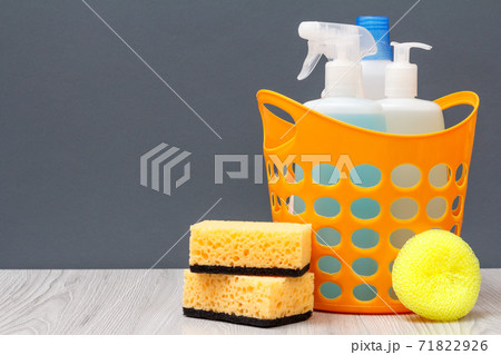 Bottles of dishwashing liquid in a basket and sponges on gray background. Bottles of dishwashing liquid in a basket and sponges on gray background. 71822926