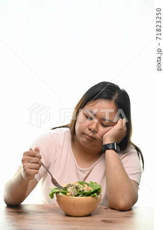 Portrait of overweight woman is tired of diet restrictions eating green salad sitting at table. Portrait of overweight woman is tired of diet restrictions eating green salad sitting at table. 71823250