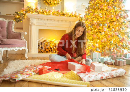 Dark-haired young woman packing christmas gifts and looking excited Dark-haired young woman packing christmas gifts and looking excited 71823930