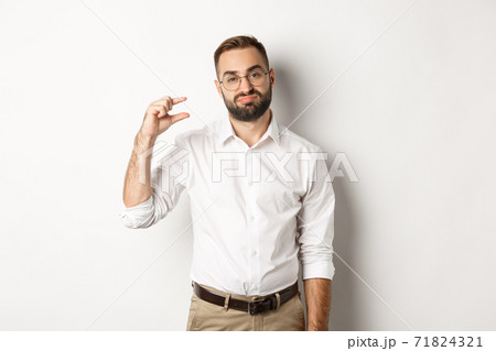 Disappointed male entrepreneur showing small object and sighing, standing over white background Disappointed male entrepreneur showing small object and sighing, standing over white background 71824321
