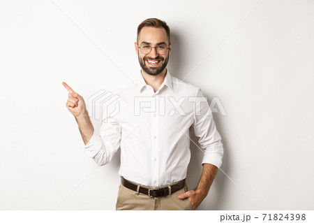Confident businessman pointing finger left at company logo, standing over white background Confident businessman pointing finger left at company logo, standing over white background 71824398