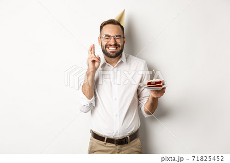 Holidays and celebration. Happy man making wish on birthday cake, cross fingers and smiling excited, having b-day party, white background Holidays and celebration. Happy man making wish on birthday cake, cross fingers and smiling excited, having b-day party, white background 71825452