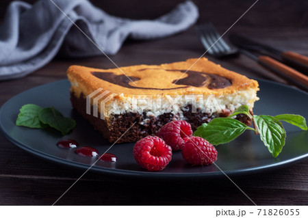 A piece of double-layer cake on a plate of chocolate brownies and curd cheesecake with raspberries. Dark background copy space A piece of double-layer cake on a plate of chocolate brownies and curd cheesecake with raspberries. Dark background copy space 71826055