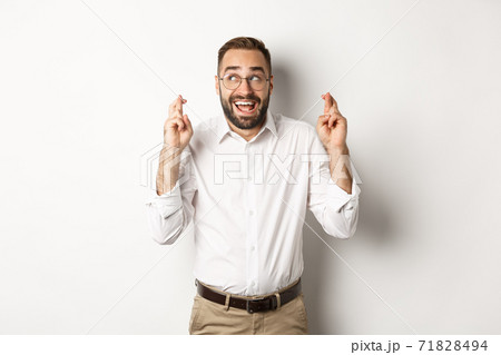 Excited and hopeful businessman making a wish, cross fingers and waiting, standing over white background 71828494
