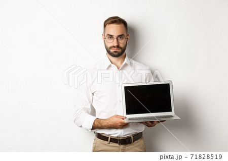 Confident manager demonstrating presentation on screen, showing laptop display and looking serious, standing over white background Confident manager demonstrating presentation on screen, showing laptop display and looking serious, standing over white background 71828519