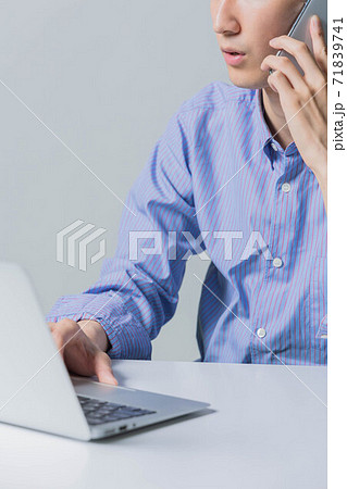 パソコンをしながらスマホで電話をする若い男性 71839741