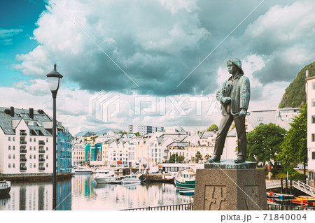 Alesund, Norway. Statue Of Young Sailor-fisher Boy On Brosundet Canal. Old Wooden Houses In Summer Day Alesund, Norway. Statue Of Young Sailor-fisher Boy On Brosundet Canal. Old Wooden Houses In Summer Day 71840004