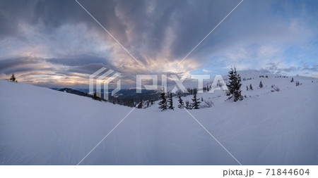 Picturesque winter windy and cloudy morning alps. Ukrainian Carpathians highest ridge Chornohora with peaks of Hoverla and Petros mountains. View from Svydovets ridge  Dragobrat ski resort. 71844604