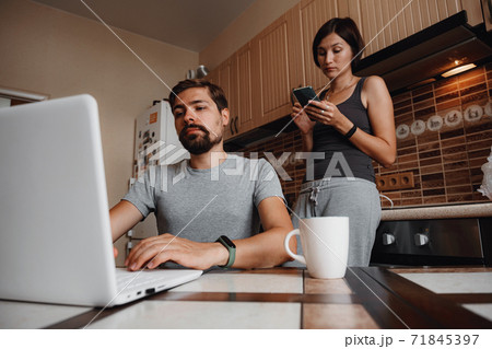 Couple at kitchen, reading news and using laptop. Couple at kitchen, reading news and using laptop. 71845397