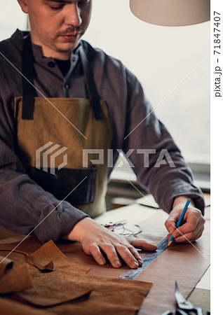 A young apprentice takes measurements on leather in the workshop on the table with a ruler A young apprentice takes measurements on leather in the workshop on the table with a ruler 71847407