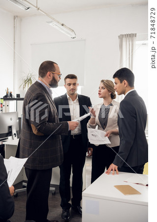The Director of the company in a jacket gives instructions and tasks to young colleagues in the office of a trading company. 71848729