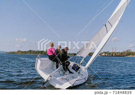 A beautiful white yacht is sailing in the wind on the river against the background of a beautiful autumn forest. A guy on board with two girls. A beautiful white yacht is sailing in the wind on the river against the background of a beautiful autumn forest. A guy on board with two girls. 71848839