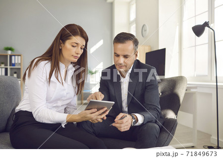 Male and female office workers sitting with a digital tablet and checking workflows in the office. Male and female office workers sitting with a digital tablet and checking workflows in the office. 71849673