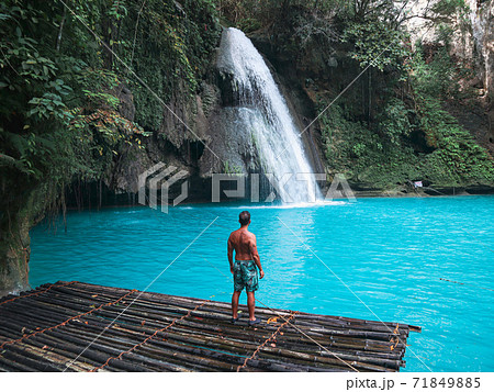 Fit man alone on the bamboo raft in front of the waterfall with turquoise water in Kawasan Falls in Cebu Island, Philippines 71849885