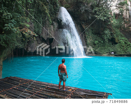 Fit man alone on the bamboo raft in front of the waterfall with turquoise water in Kawasan Falls in Cebu Island, Philippines 71849886