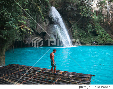 Fit man alone on the bamboo raft in front of the waterfall with turquoise water in Kawasan Falls in Cebu Island, Philippines 71849887