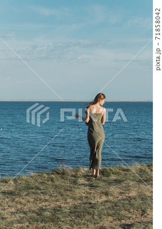 View from the back of a girl in a long dress, standing on a cliff and admiring the beautiful view of the lake. 71858042