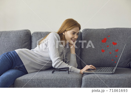 Happy young woman lying on sofa with laptop, video calling her boyfriend or chatting online 71861693