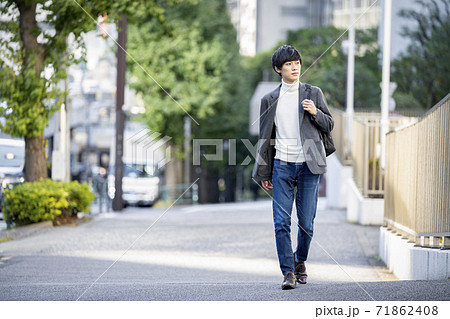バックパックを持って歩道を歩く若い男性の写真素材