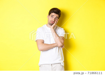 Bored and gloomy guy looking up, imaging things, standing over yellow background 71866111
