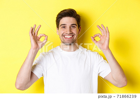 Close-up of handsome young man showing okay sign, approve and agree, smiling satisfied, standing over yellow background Close-up of handsome young man showing okay sign, approve and agree, smiling satisfied, standing over yellow background 71866239