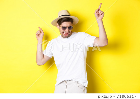 Tourism, travelling and holidays concept. Male tourist enjoying vacation, dancing in straw hat and sunglasses, pointing fingers sideways 71866317