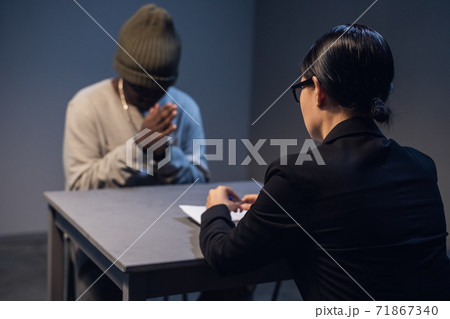 At the police station, a girl investigator interrogates a black guy who is sitting in front of her in handcuffs At the police station, a girl investigator interrogates a black guy who is sitting in front of her in handcuffs 71867340