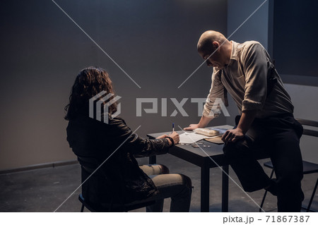 At the police station, the criminal caught red-handed signs documents, the investigator sits on the table 71867387