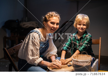 a young mother and her young son pose for a photo in a pottery workshop, modeling dishes from clay. 71867634