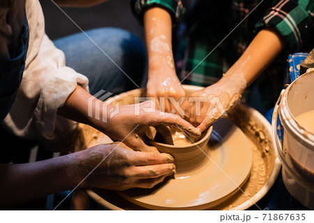 the process of modeling clay dishes on a potter's wheel, the hands of a young girl and a child. 71867635