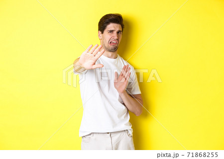 Disgusted man refusing, grimacing from dislike and aversion, begging to stop, standing in white t-shirt against yellow background 71868255