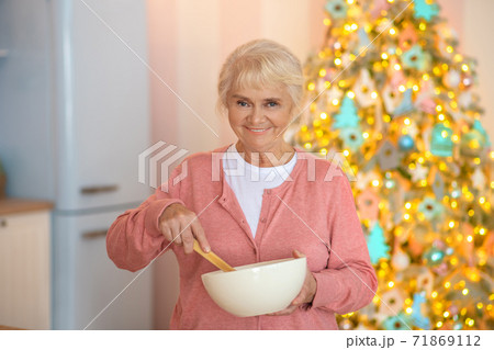 Smiling grey-haired woman stirring something in a bowl 71869112