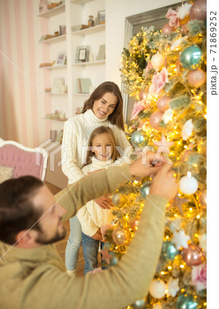 Dad putting balls on christmas tree while his wife and daughter watching him Dad putting balls on christmas tree while his wife and daughter watching him 71869252