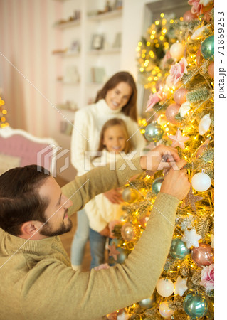 Dad putting balls on christmas tree while his wife and daughter watching him 71869253