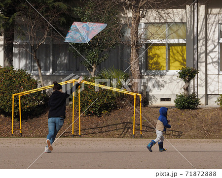 小学校の校庭で凧揚げをする親子 71872888