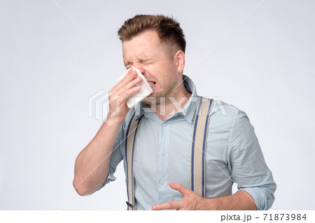 Young caucasian man covering his nose with handkerchief sneezing. Young caucasian man covering his nose with handkerchief sneezing. 71873984