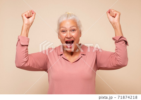 Happy middle aged caucasian woman raising fists in winning gesture and celebrating success Happy middle aged caucasian woman raising fists in winning gesture and celebrating success 71874218