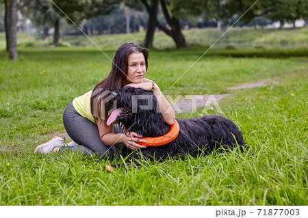 Girl hugs black long-haired dog while walking in park. 71877003