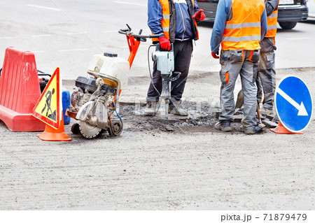 A team of road workers equipped with an electric jackhammer, a gas cutter, a shovel and a brush discusses a road section repair plan. 71879479