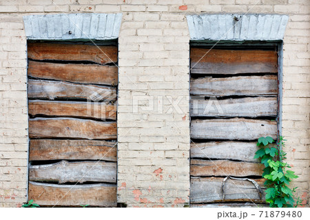 The window openings of the dilapidated house are boarded up with old boards. The window openings of the dilapidated house are boarded up with old boards. 71879480