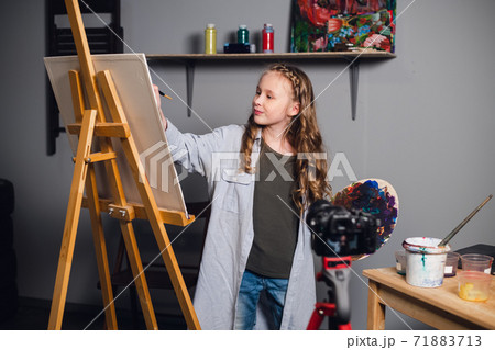 a cute teen artist is recording a story for her video blog in a workshop at an art school. 71883713