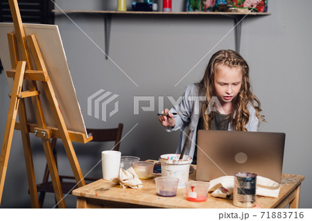 cute girl artist draws her oil painting from a reference from a laptop. 71883716