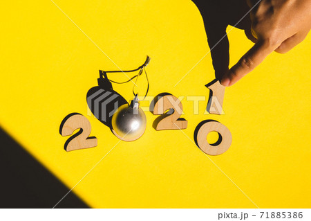 Wooden numbers 2021 chainging 2020 with child hand and a silver christmas ball on a yellow background. Wooden numbers 2021 chainging 2020 with child hand and a silver christmas ball on a yellow background. 71885386