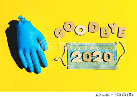Words GOODBYE 2020 from wooden letters on a yellow background, inflated medical glove and facemask. 2020 and epidemic concept. Words GOODBYE 2020 from wooden letters on a yellow background, inflated medical glove and facemask. 2020 and epidemic concept. 71885388
